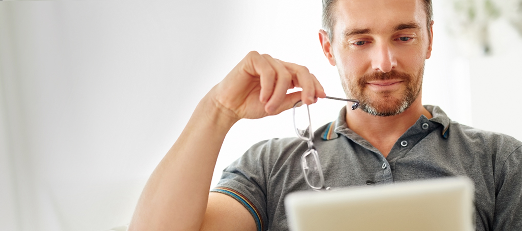 Man holding eye glasses looking at a tablet.