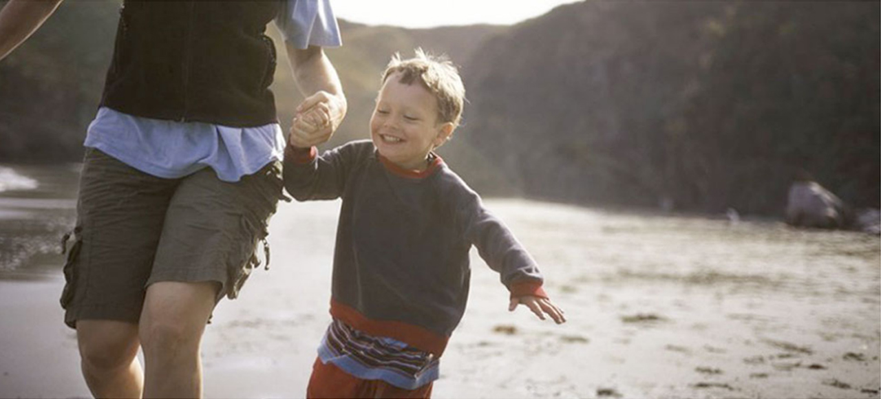 A child holding an adults hand near a river.